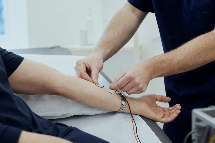 Clinician placing a small surface electrode on a patient's forearm before a nerve conduction study
